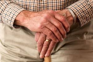 Older man's hands crossed holing a walking stick